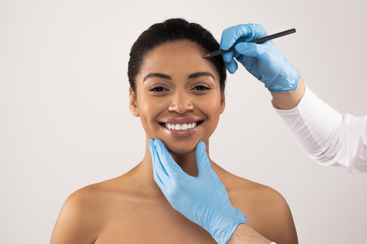 Beautitian hands making preparation lines on black woman face