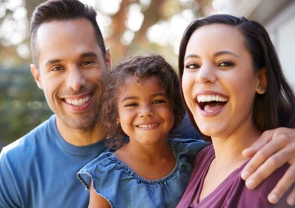 Portrait Of Smiling Hispanic Family With Daughter Laughing In Garden At Home