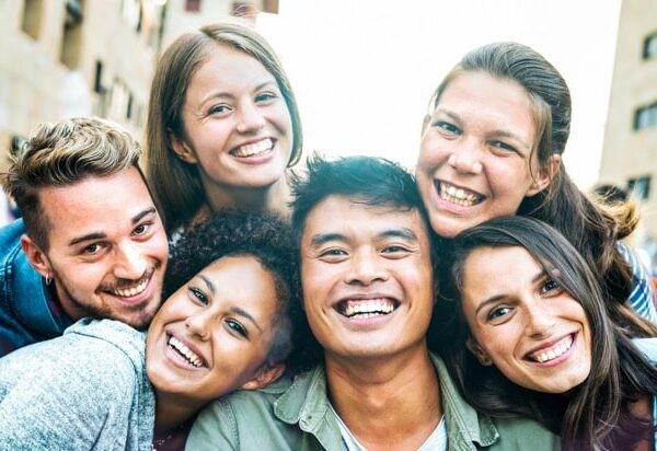 Multicultural men and women taking selfie out side with backlight - Happy milenial life style concept on young multiracial friends having fun day together - Bright azure filter with sunshine flare